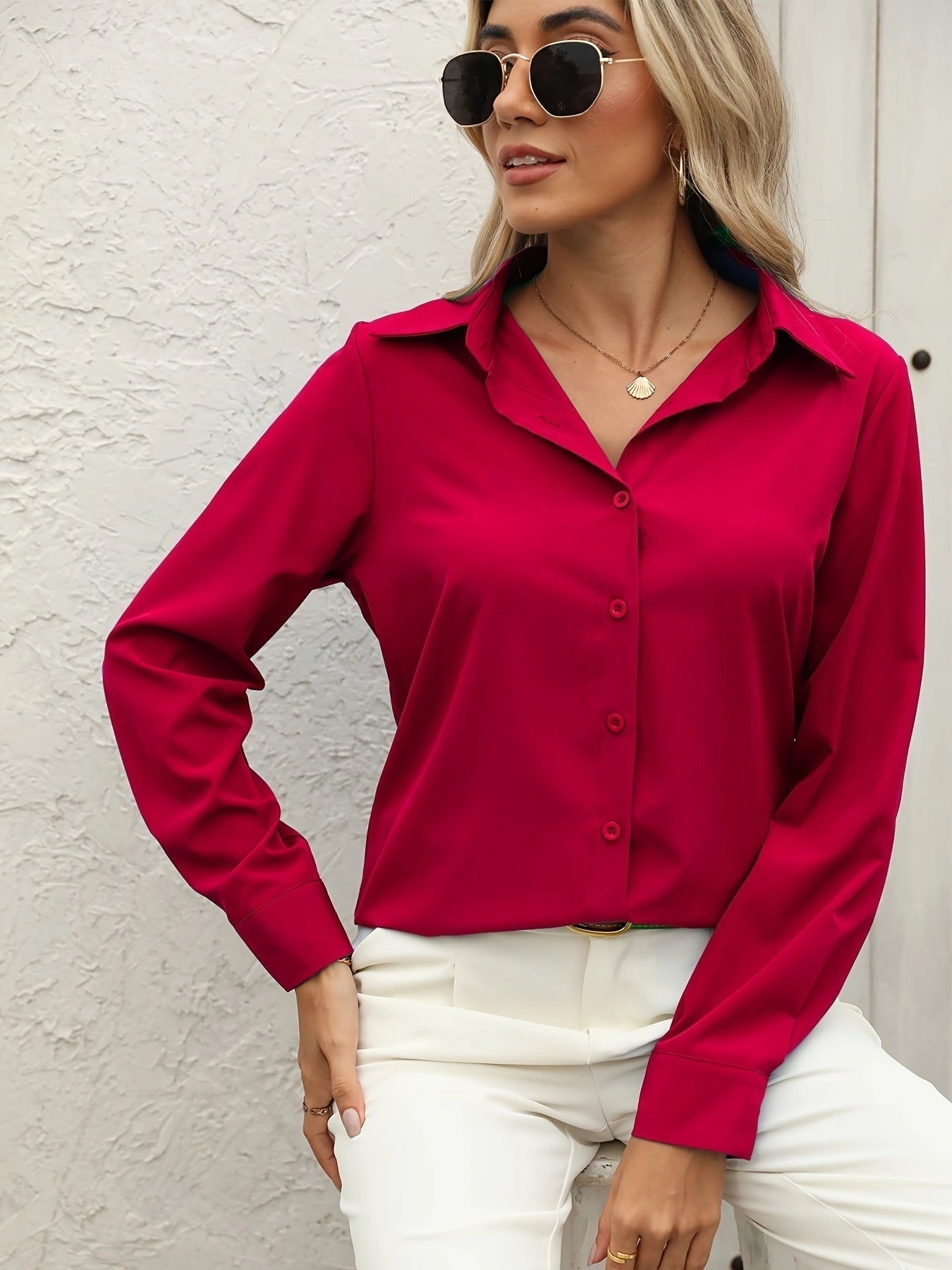 A woman wearing a crimson silk satin blouse with long sleeves, styled elegantly with sunglasses and outerwear.