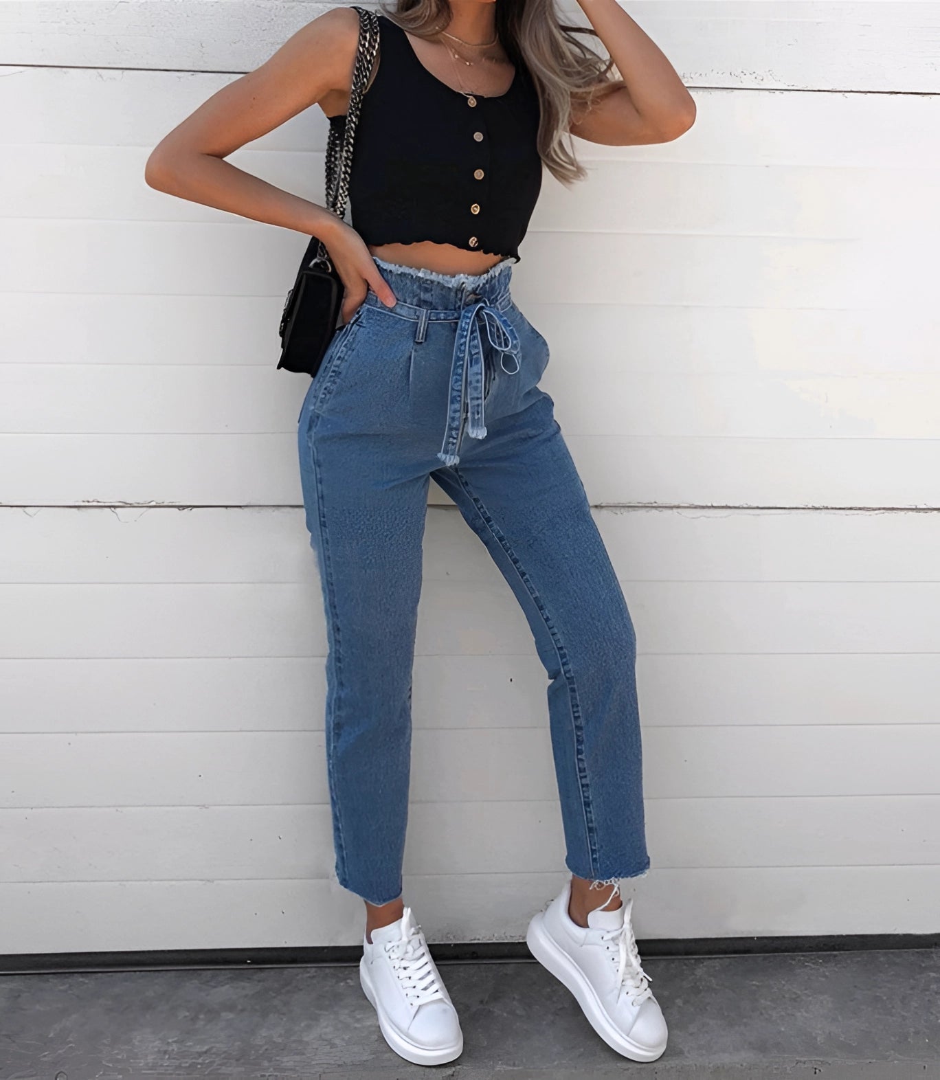 Woman wearing high-waist jeans and a cropped black tank top, showcasing trendy urban fashion.