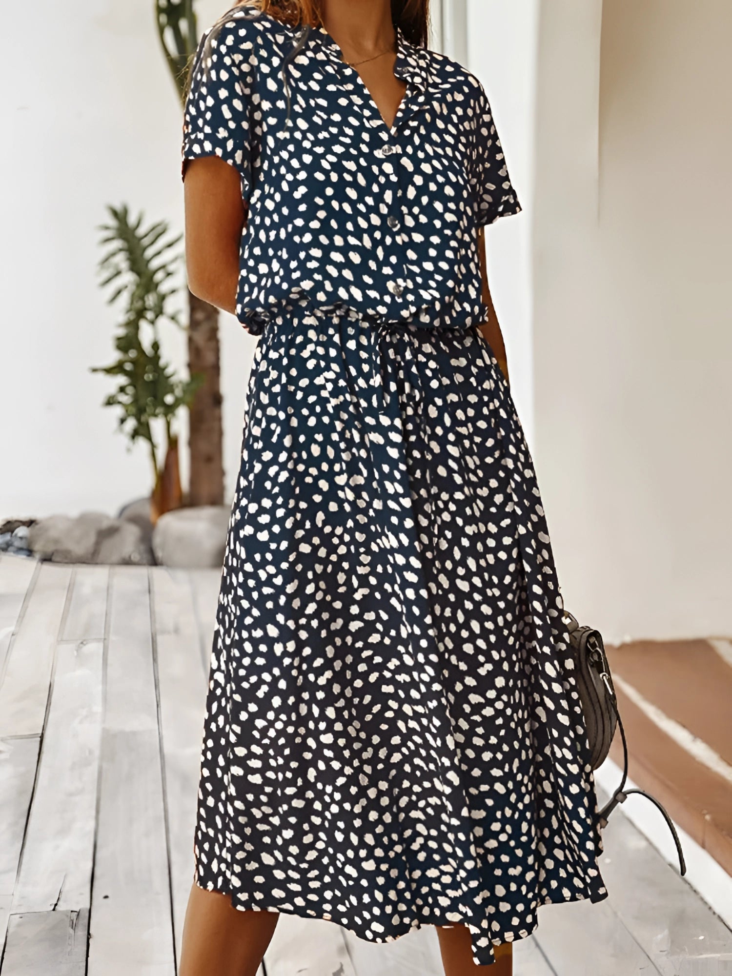 A model wearing a white polka dot midi dress with short sleeves and a tie waist, ideal for summer.