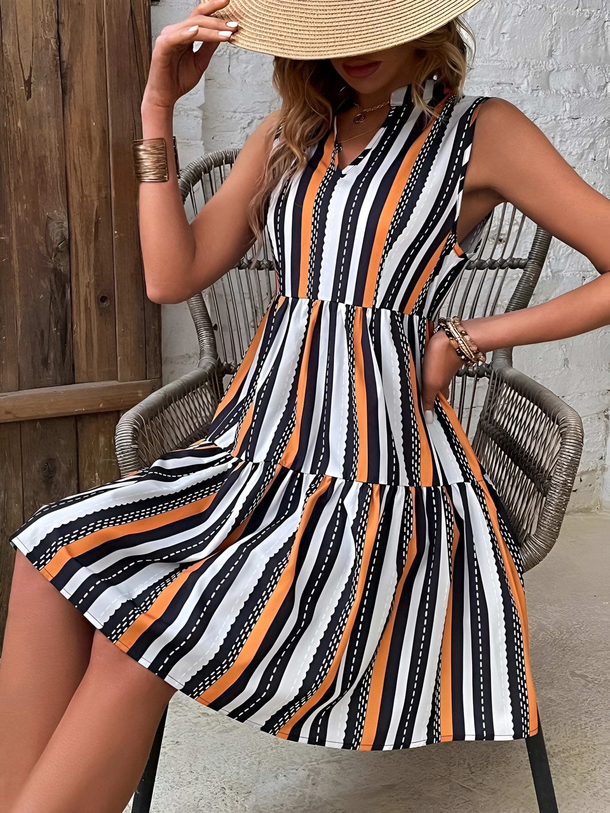 A woman wearing a striped sleeveless summer dress in black, white, and orange with an A-line cut, accessorized with a hat.