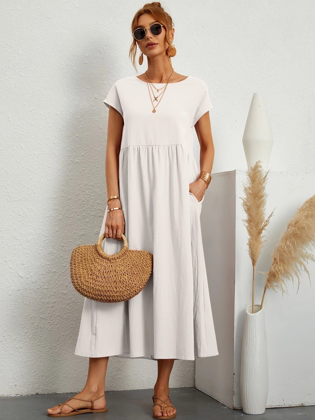 Woman wearing white midi dress with short sleeves and crew neck, suitable for casual summer outings; she is carrying a grey bag.